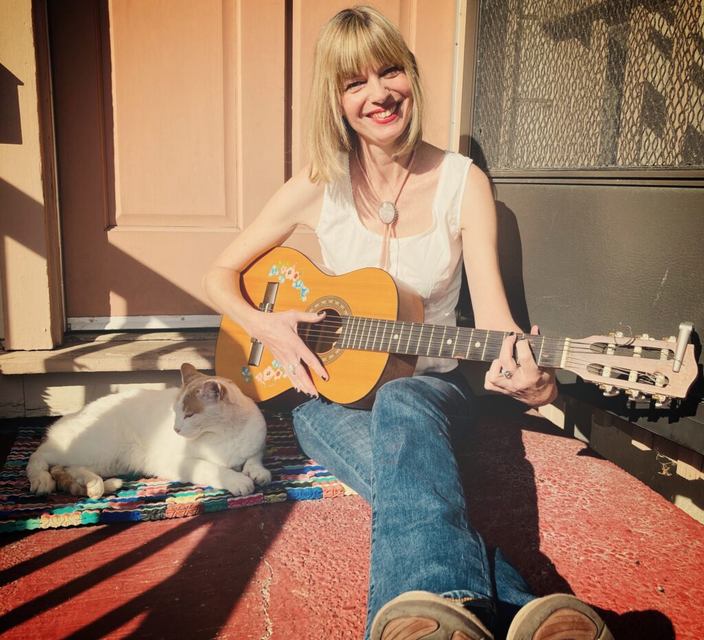 Photo of a woman with a parlor guitar and cat by her side.